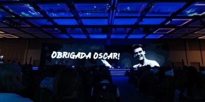 imagem de um salão iluminado em azul e ao fundo no telão a frase: Obrigada Oscar